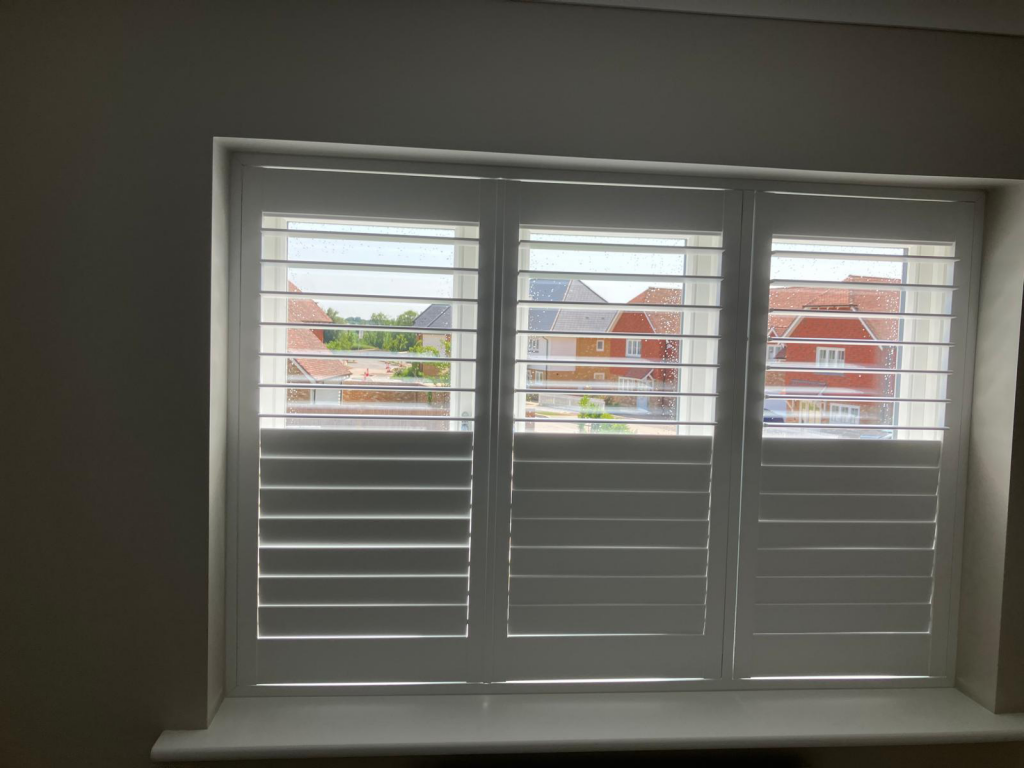 White window shutters partially open, revealing houses and cloudy sky—perfect for those seeking chic home décor or stylish blinds solutions.