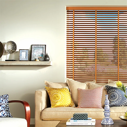 A cosy living room with beige sofa, colourful cushions, made-to-measure Venetian blinds, and a shelf with framed art and decor items.