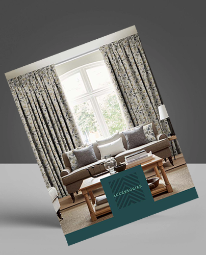 A catalogue cover featuring a living room with a sofa, patterned curtains, and cushions. A wooden coffee table sits in front, and large windows let in natural light. The word ACCESSORIES is printed at the bottom.