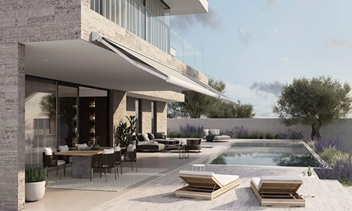Modern house with large glass windows and a patio featuring outdoor seating, dining area, and a rectangular swimming pool. Two loungers are on the poolside decking, surrounded by plants and trees under a partly cloudy sky.