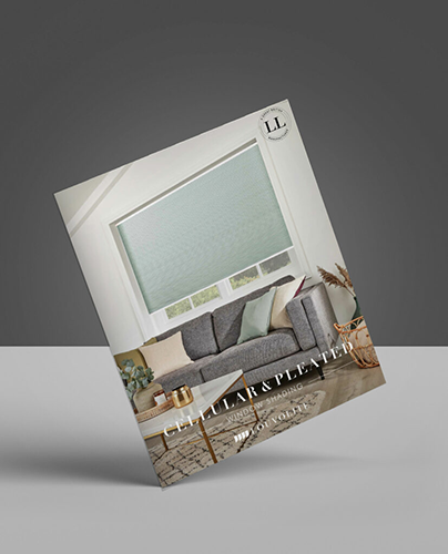 A catalogue featuring a living room with a grey sectional sofa, pastel cushions, a round coffee table, plants, and a large window with a light-coloured cellular or pleated blind on the cover.