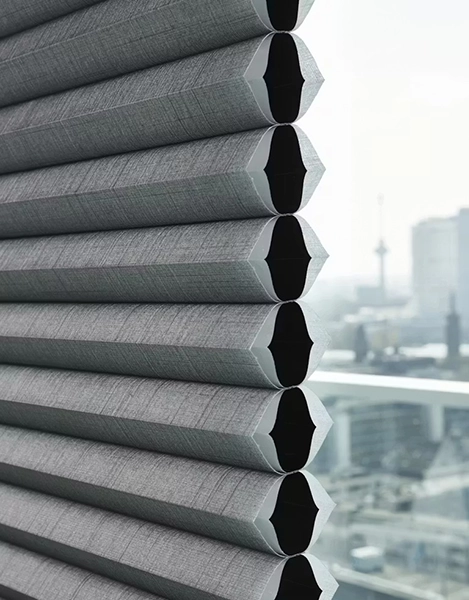 Close-up of grey Luxaflex® Duette® Blinds Kent, partially open, with a blurred cityscape and buildings visible through the window in the background.