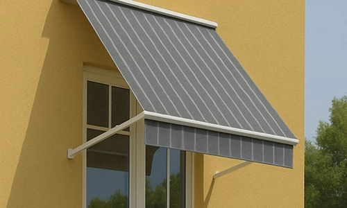 A grey striped fabric awning extends over a window on a yellow wall, providing shade. The awning is supported by white metal arms. Trees are visible in the background.