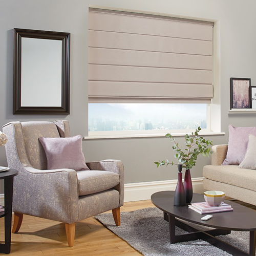 Modern living room with a grey armchair, light pink cushions, a coffee table with a plant, wall art, and a large window dressed in Made to Measure Roman Blinds. The space features soft neutrals and stylish wooden flooring.