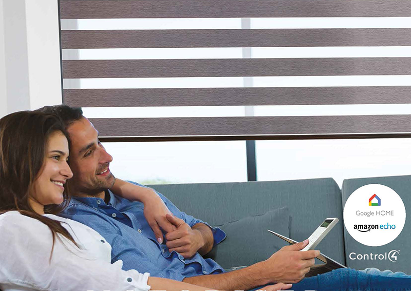 A smiling couple relaxes on a sofa, holding a remote control. Behind them are modern Made to Measure Motorised Blinds Kent. Google Home, Amazon Echo, and Control4 logos appear in the lower right corner.