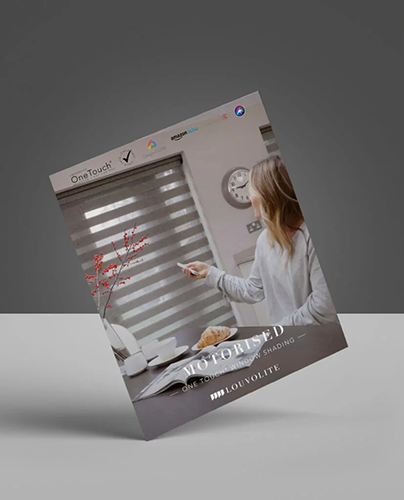 A woman sitting at a desk uses a remote control to operate motorised window blinds. The background shows a modern interior with a clock on the wall. The image is featured on a tilted magazine cover for Louvolite.