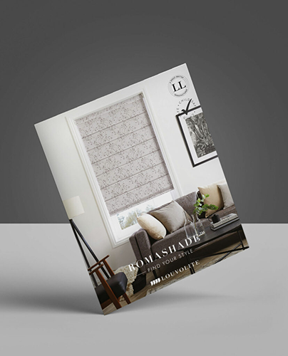 A brochure featuring a Romanesque window blind over a window in a modern living room with a grey sofa, framed wall art, and a small table. The brochure is titled ROMAN BLINDS by Louvolite.