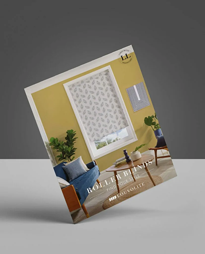 A brochure for Louvolite roller blinds stands upright, featuring a modern living room with a yellow wall, a window with patterned blinds, blue sofa, wooden coffee table, and green plants.