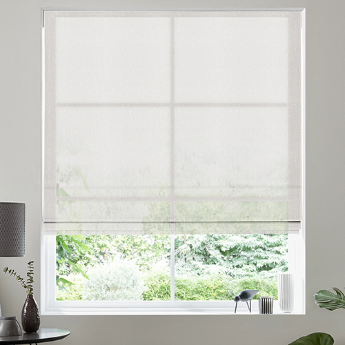 A large window with a voile roller blind partially lowered, letting in natural light. Outside, green foliage is visible. Inside, there is a black lamp, a small bird figurine, and a plant on the windowsill.