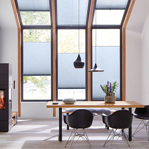 Modern dining area with large floor-to-ceiling windows, VS2 Slide Comfort Blind, a wooden table, black chairs, pendant lights, a potted plant centrepiece, and a fireplace on the left. Natural light fills the space.