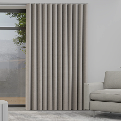 A modern lounge with a light grey armchair and floor-to-ceiling grey vertical blinds, complemented by made-to-measure curtains, covering a large window that partially reveals an outdoor scene with lush greenery.