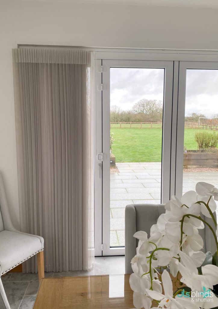 Sheer vertical blinds partially cover glass patio doors, with a view of a green lawn and cloudy sky outside. White orchid in foreground.
