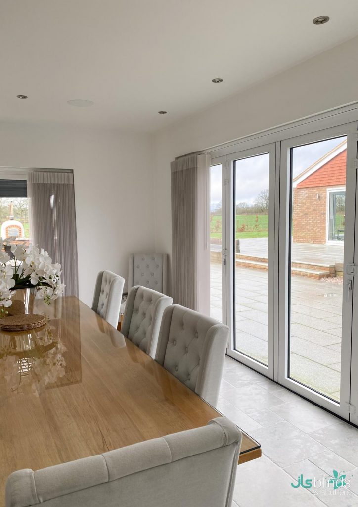 Modern dining area with a wooden table, upholstered chairs, and large glass doors opening to a patio with a garden view.