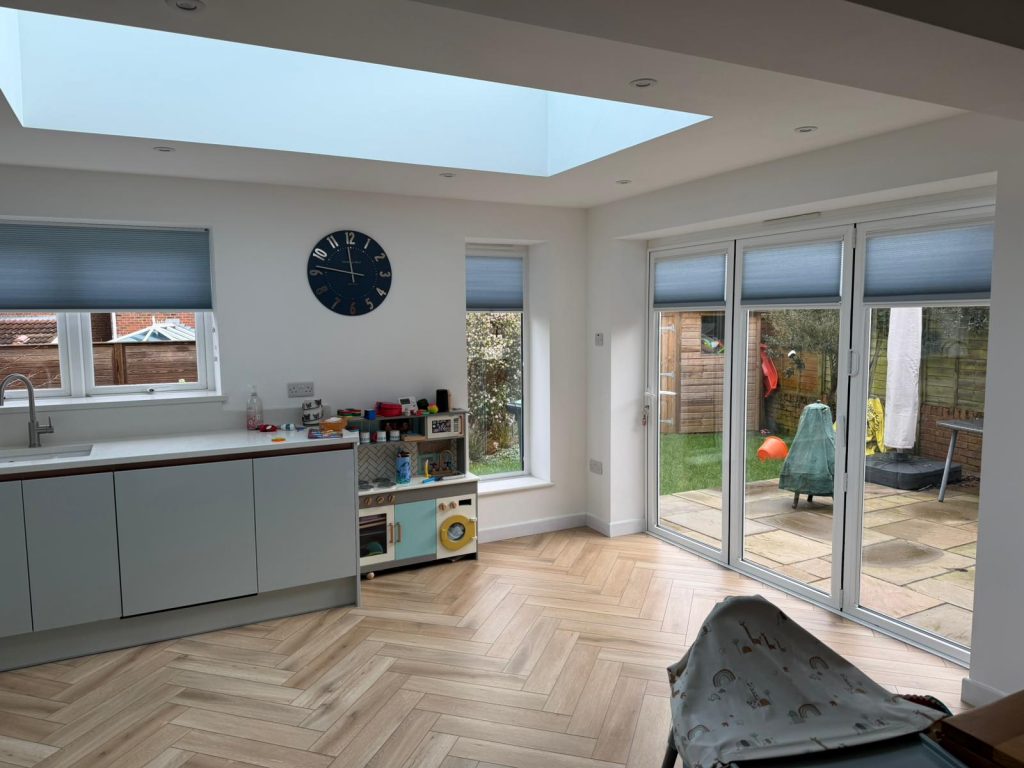 Bright, modern kitchen with toys, play kitchen, large glass doors, skylight, and view of a patio and garden outside.