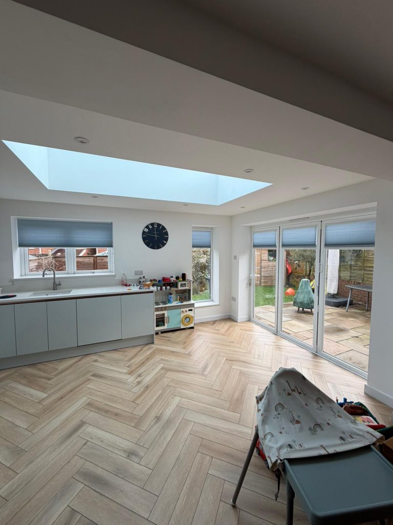 Modern kitchen with herringbone wood floor, skylight, toy kitchen, and large glass doors opening to a patio and garden.