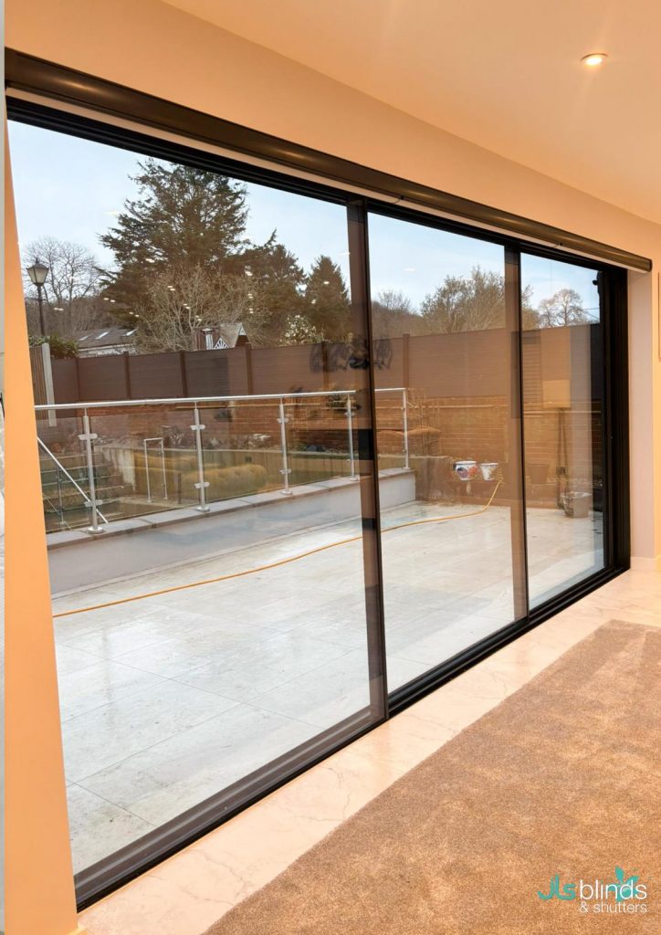 Large sliding glass doors with black frames open to a patio, showing a view of a landscaped garden and trees outside.