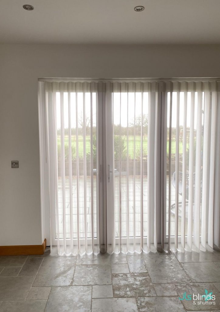 Vertical white blinds cover large glass patio doors, letting in natural light and revealing a view of a green lawn outside.